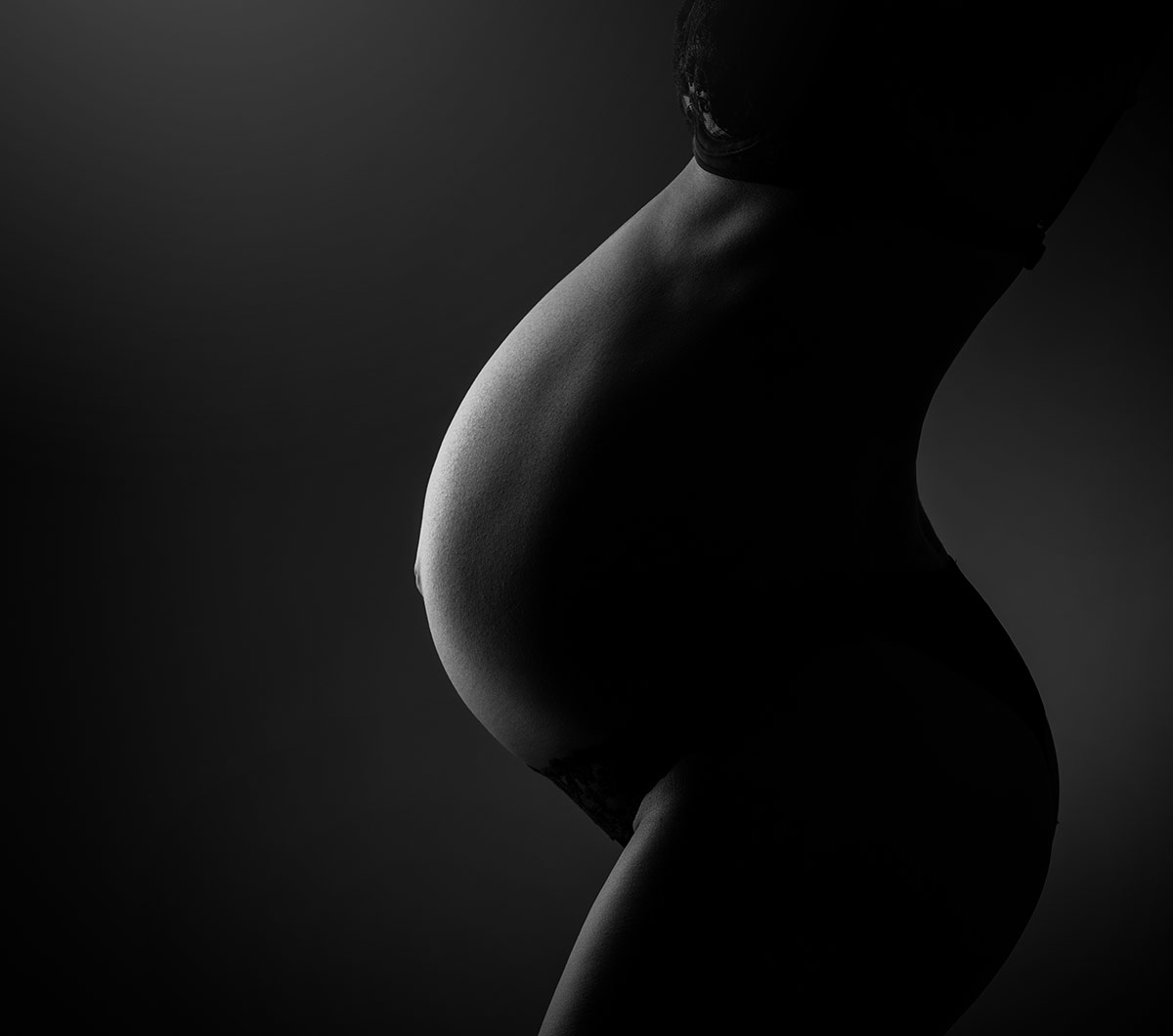 closeup silhouette of pregnant belly on black