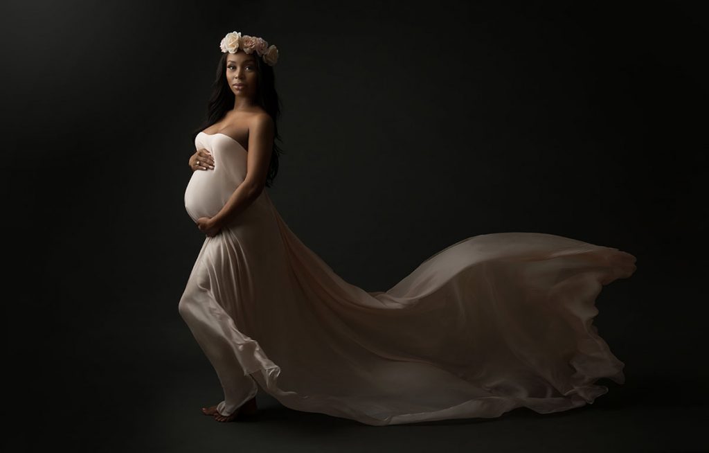 maternity photography of model flowing fabric and floral crown on black