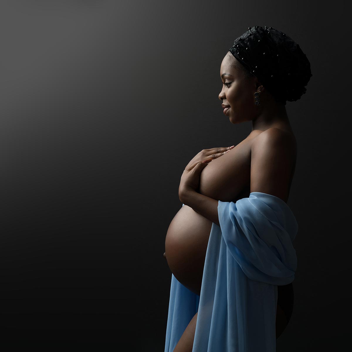 fine art portrait of pregnant women with blue fabric photographed on black backdrop
