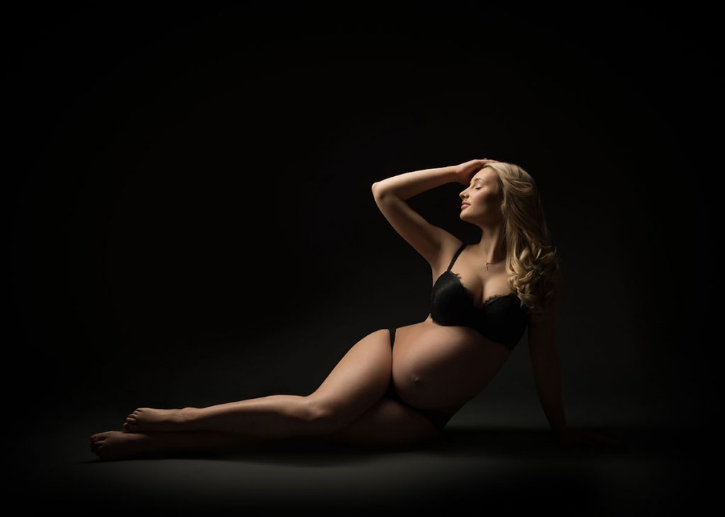 pregnant woman laying down on black backdrop in Midtown photography studio