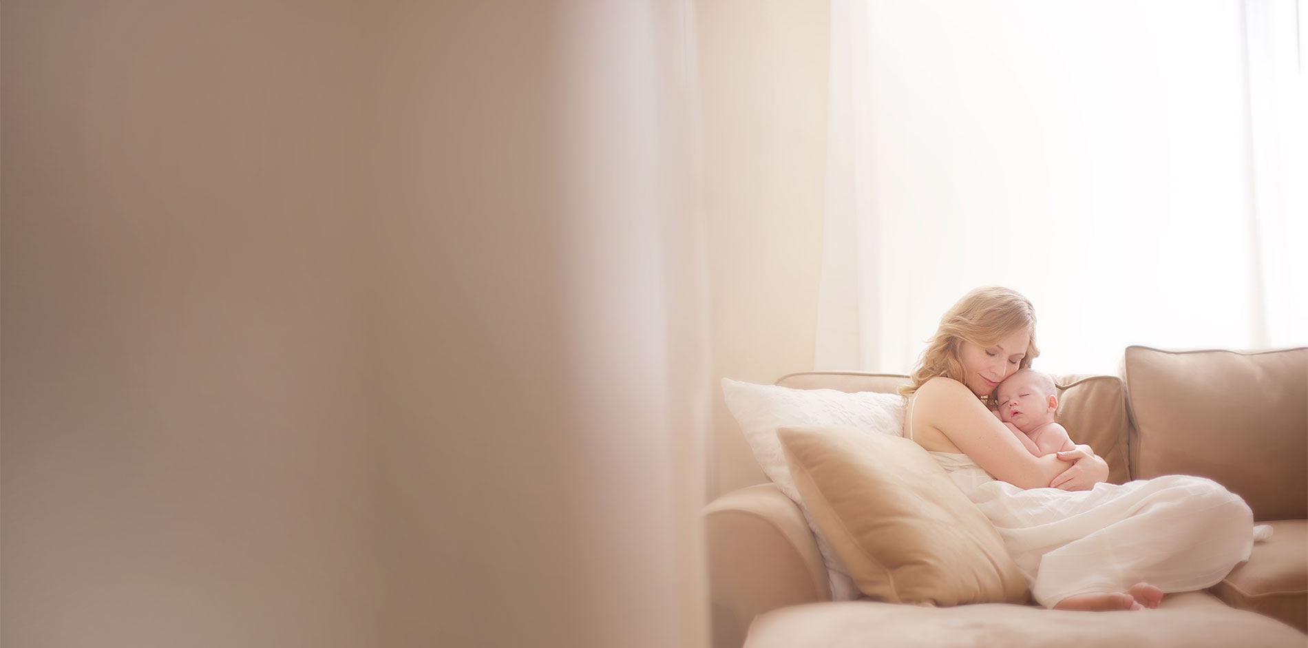 Mom cuddling her baby on a couch in a modern room.