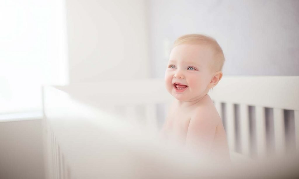 Smiling baby standing in a crib.