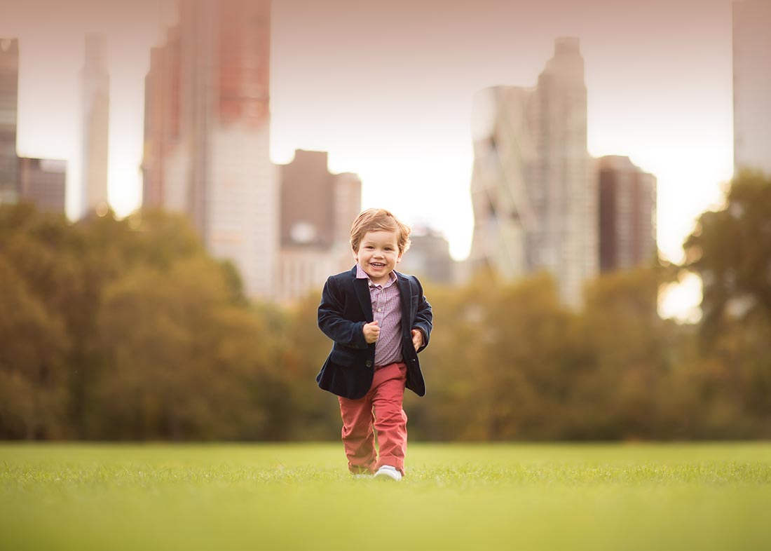 Stylish toddler running through a grass field in NYC's Central Park.