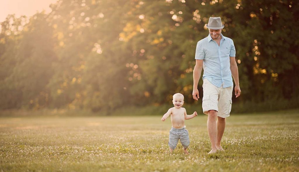 A father walking with his baby son in a field full of clovers.