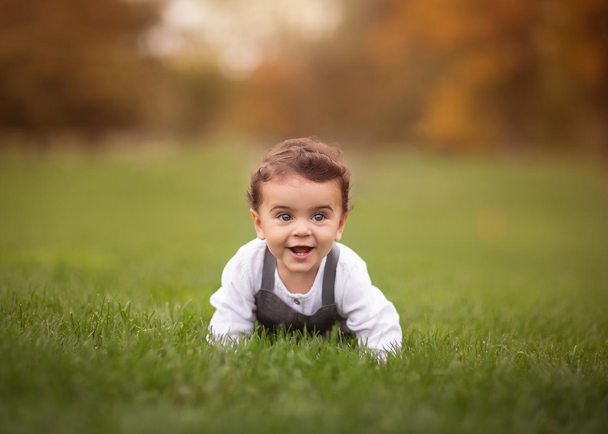 Happy toddler crawling through grass while smiling.