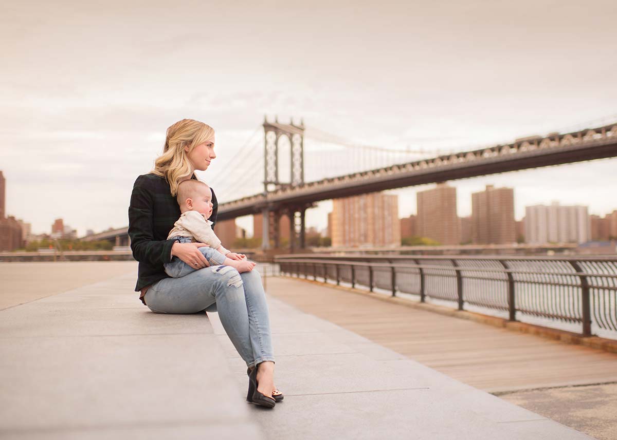Mother and her baby boy in Brooklyn Bridge Park, with Manhattan Bridge in the background.