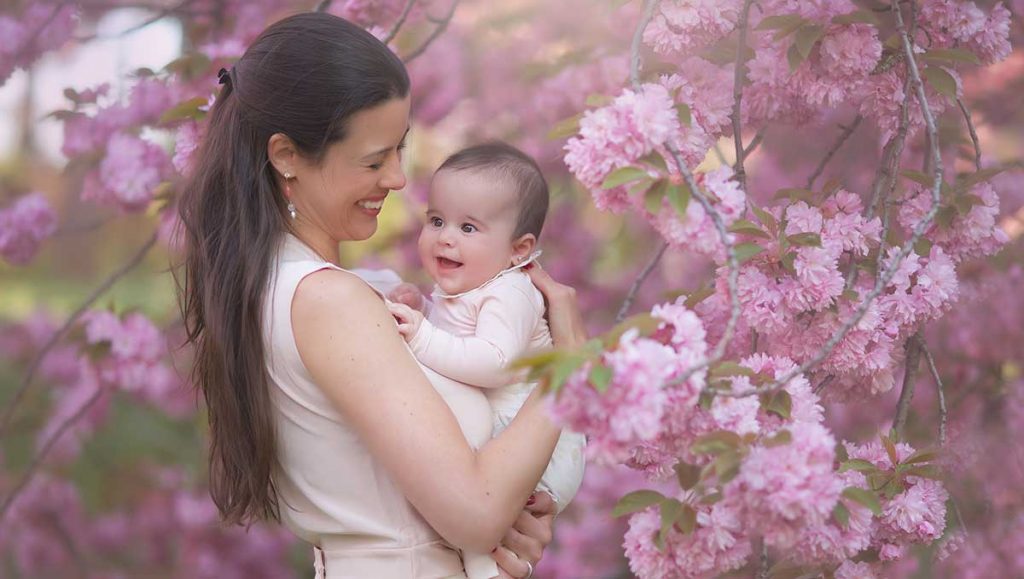 Mother holding her baby girl amongst cherry blossom trees.