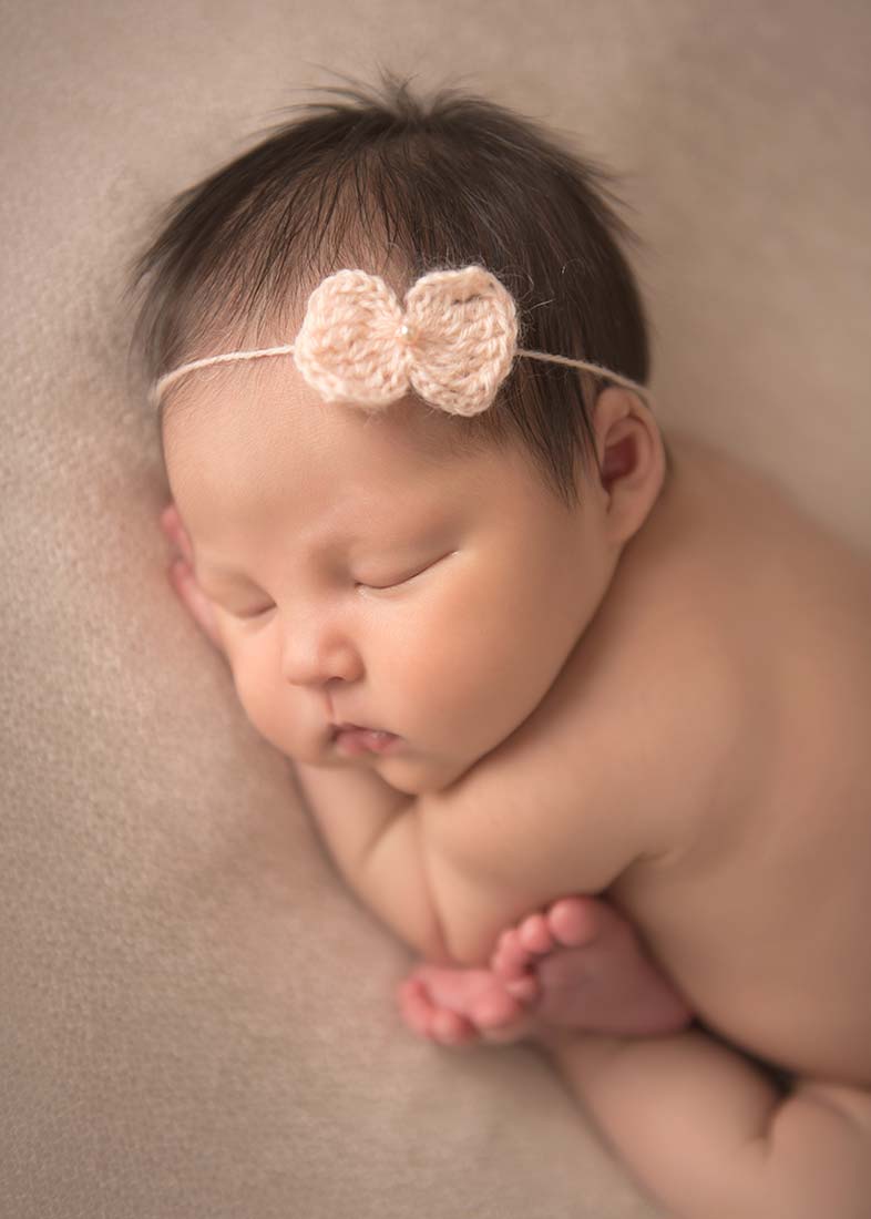 cute baby girl with peach headband in cozy newborn pose