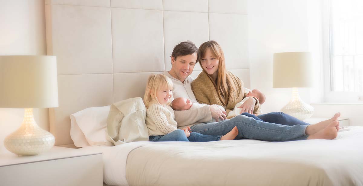 Mother holding her newborn baby on a bed along with her husband and daughter