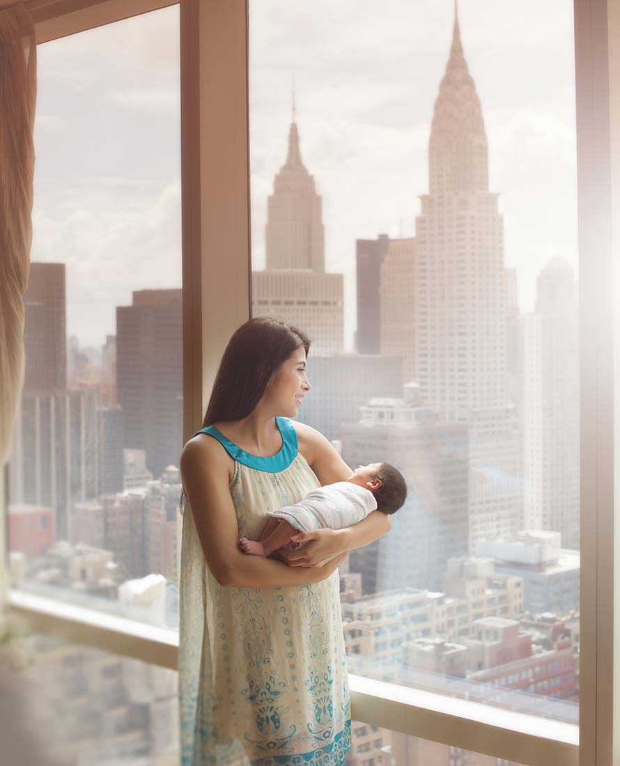 Mother holding her newborn baby near a window with a beautiful view of the NYC skyline
