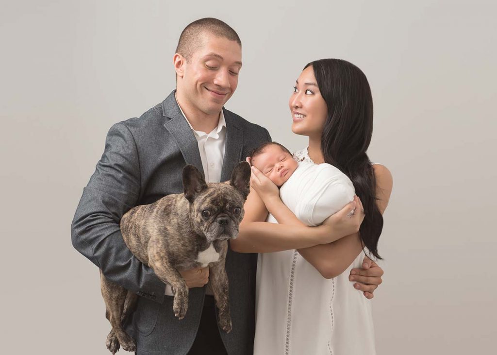 Happy married couple holding their baby and their dog while posing for a family portrait