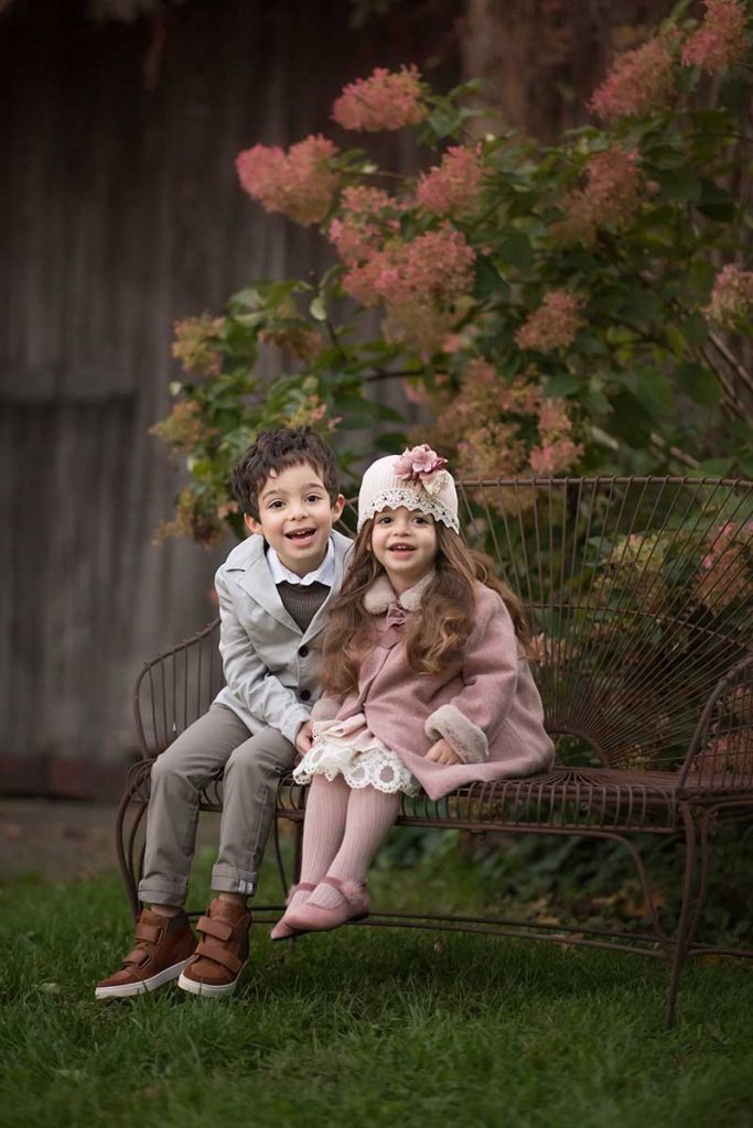 Siblings dressed in stylish clothes sitting on a bench smiling