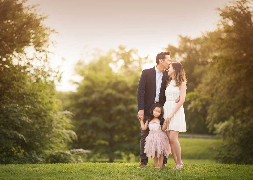 A kissing portrait of a family and their young daughter in Central Park