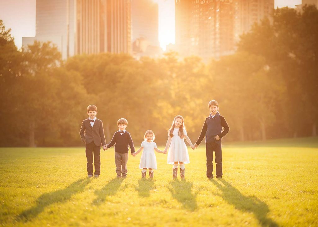 Five siblings dressed stylishly holding hands during sunset in Central Park NYC