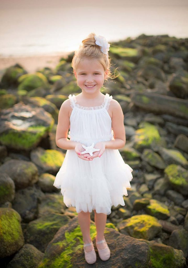 Girl in a white tutu posing on rocks at a beach