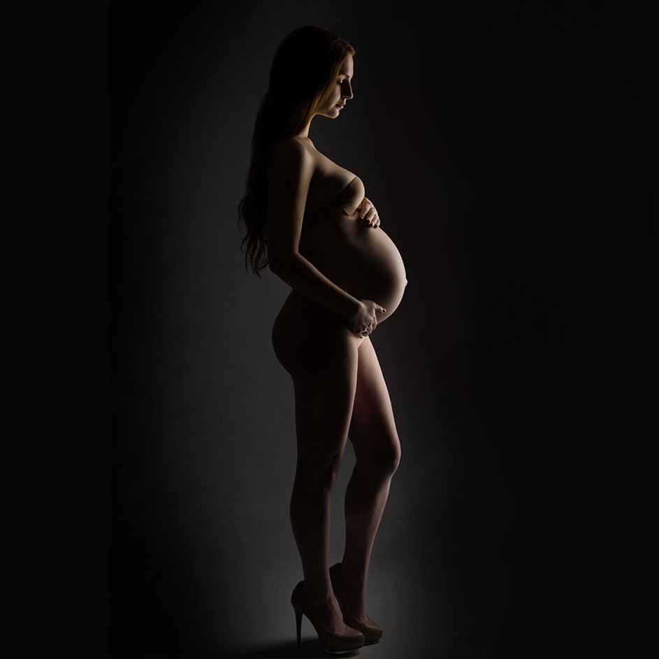 Profile of a pregnant woman in a studio, cradling her belly.