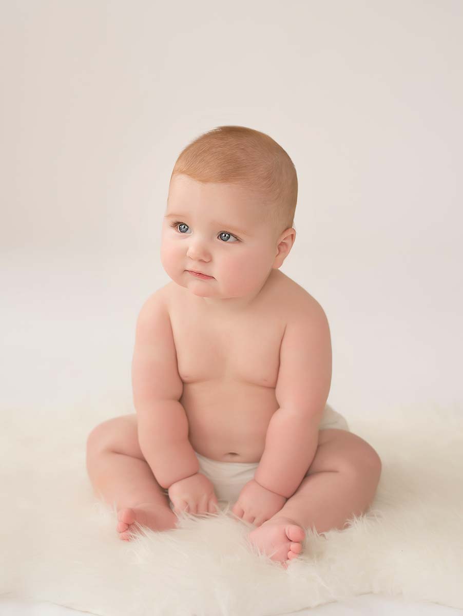 Chubby baby sitting on a white rug at a photo studio in NYC