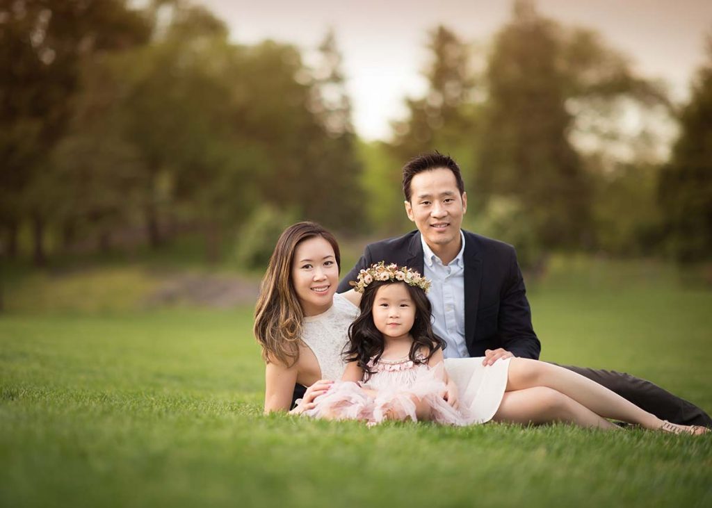 Husband and wife sitting with their daughter in a grass field