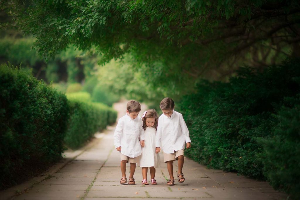 Three siblings walking through a garden