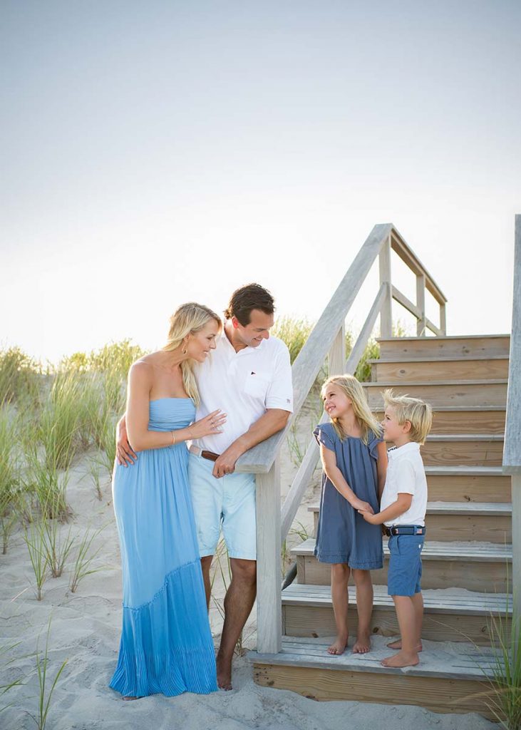 Brother and sister hold hands while sharing a smile with their Mom and Dad on a beach in the Hamptons