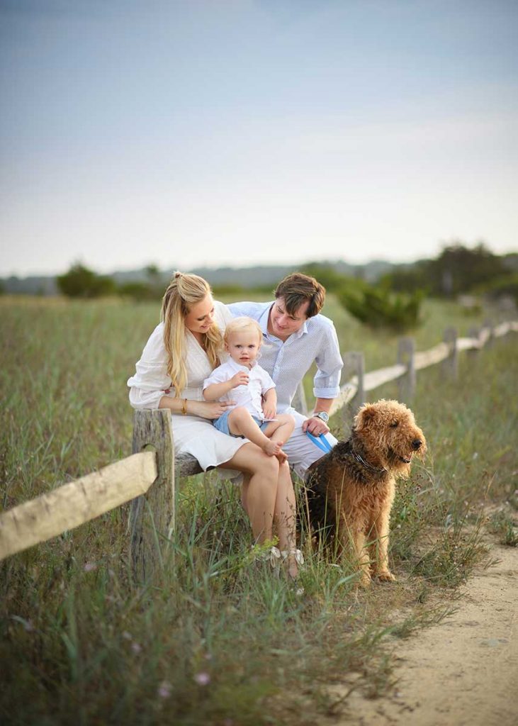 A family from the Hamptons sitting on a farm fence along with their baby and family pet