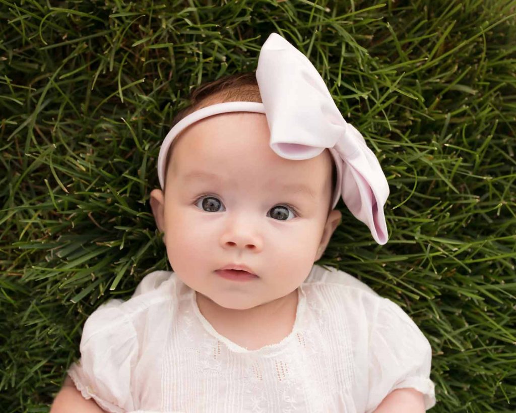 Baby girl with headband laying in grass