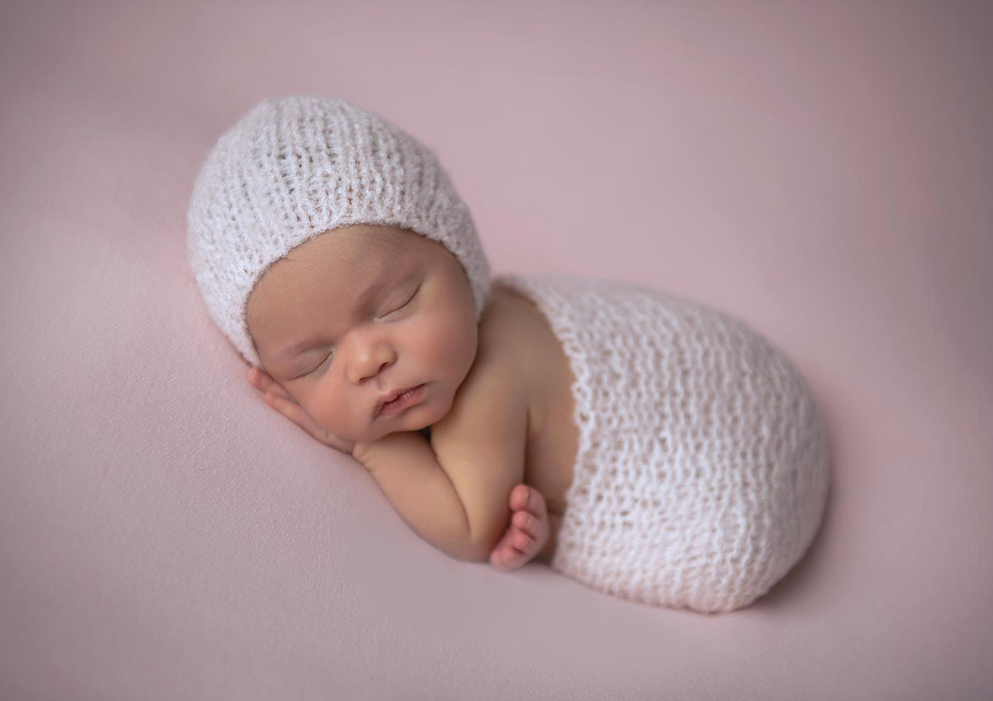 newborn girl sleeping in soft pink knit wrap and bonnet