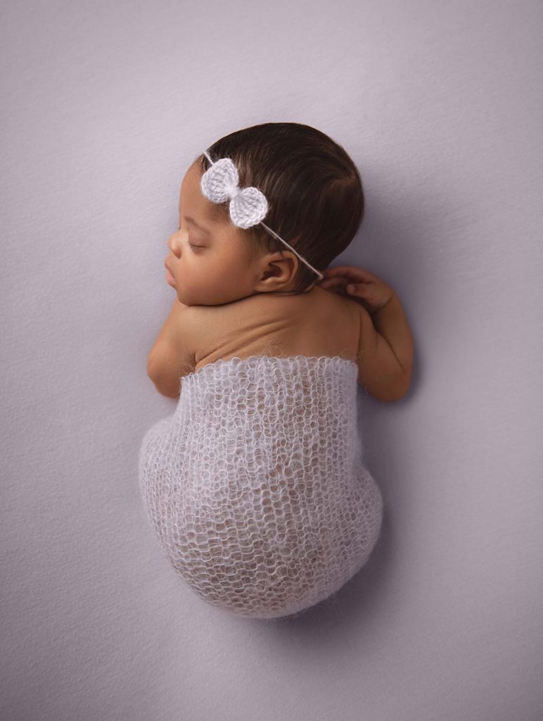newborn sleeping on lilac purple blanket with bow headband for studio photo shoot