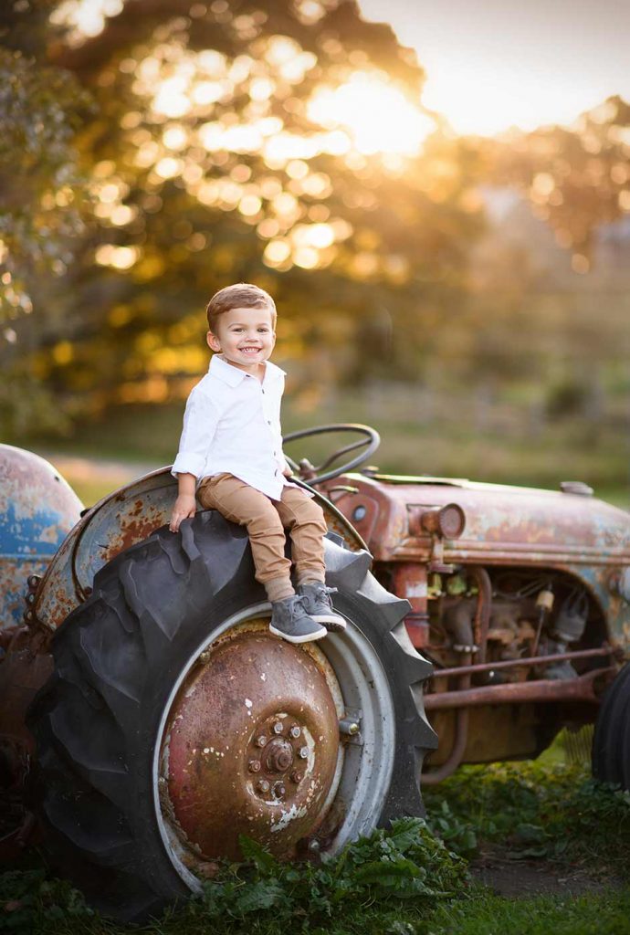 Boy sitting on a rusty tractor during sunset