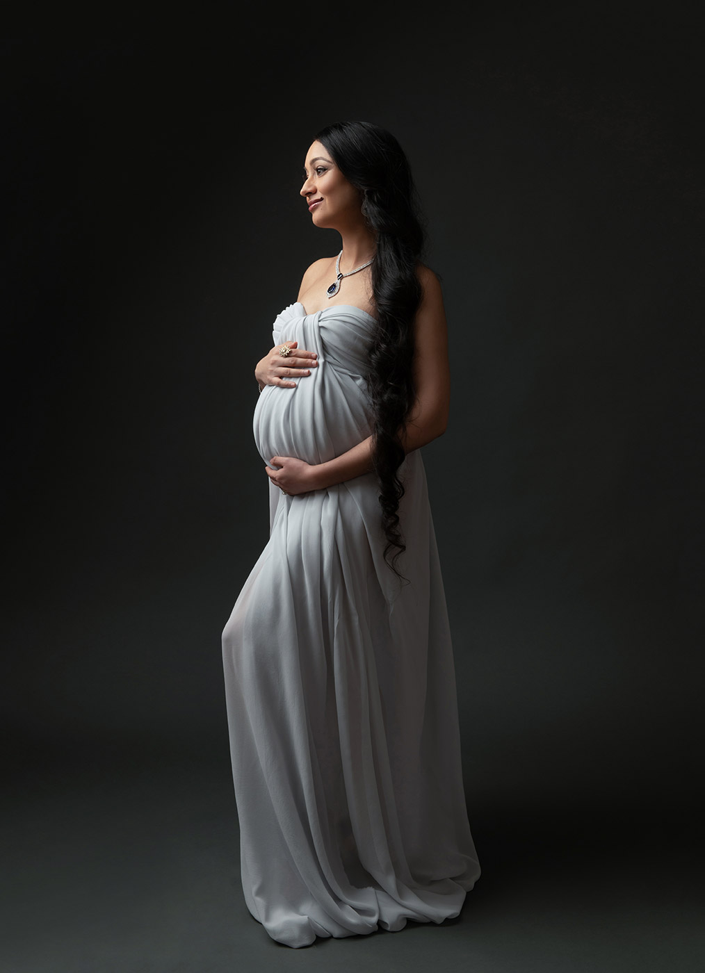 pregnant woman with long black hair and blue silk gown posing for studio silhouette