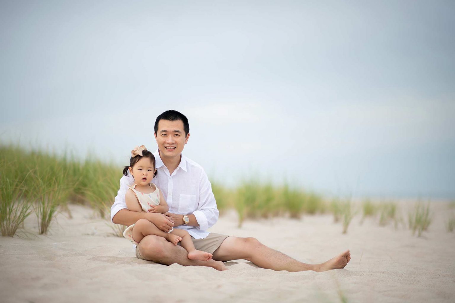 Happy father sitting with his daughter in sand near Amagansett, NY