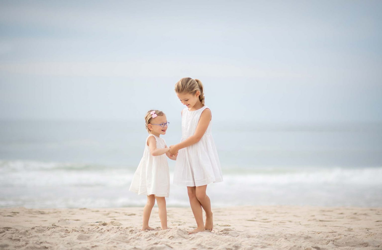 Two sisters in white dresses dancing on a beach in Southampton NY