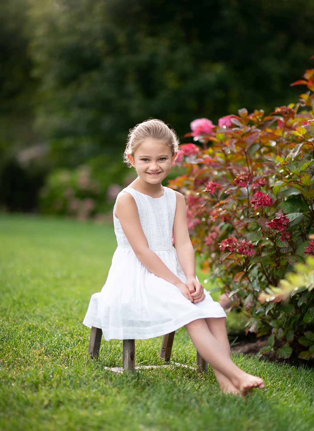Girl in a white dress sitting on a bench in her Bridgehampton NY backyard