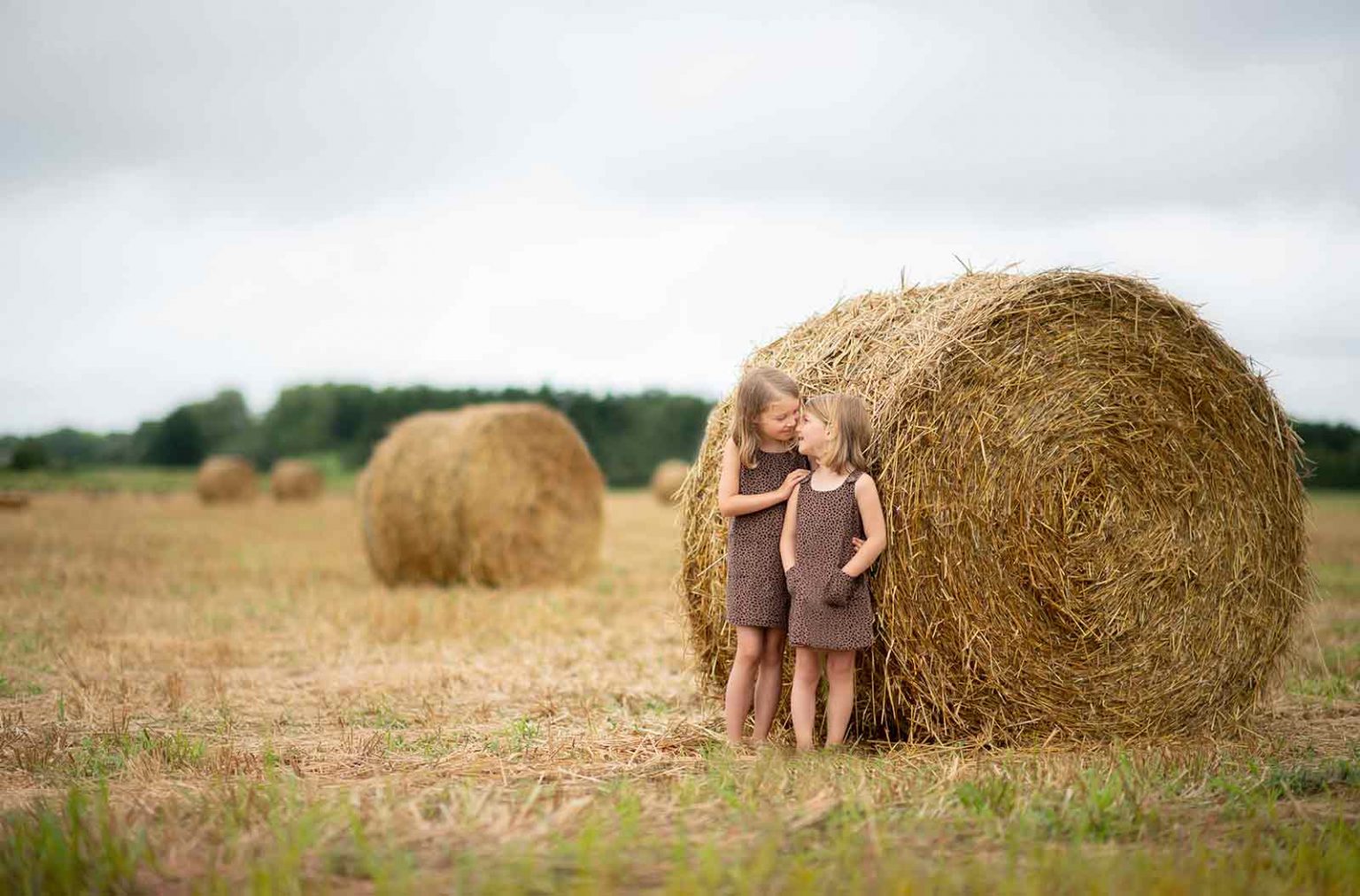Sisters bonding on a farm in the Hamptons with rolled hay in the background
