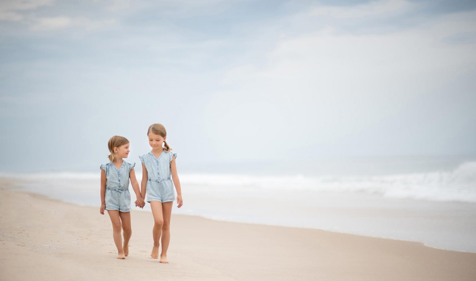 Two young girls holding hands on a beach