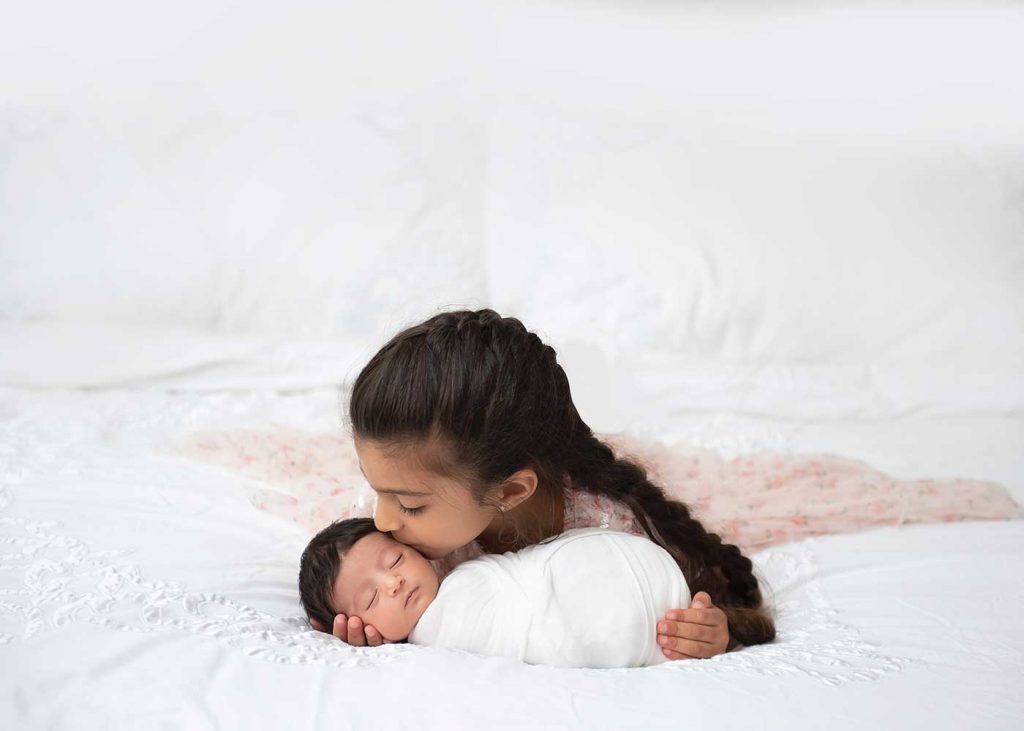 Girl kissing her baby brother on the bed of their NYC home