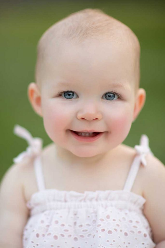 Blue eyed toddler smiling for a baby photographer in NYC
