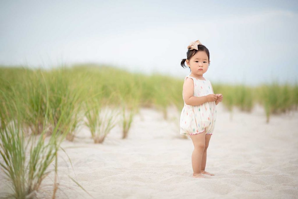 Toddler girl in a dress playing in sand at a beach near East Hampton NY