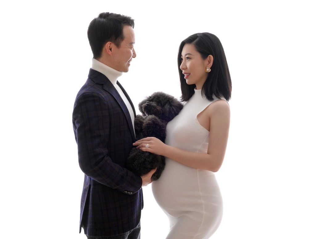 Married couple posing for a pregnancy photo along with their pet