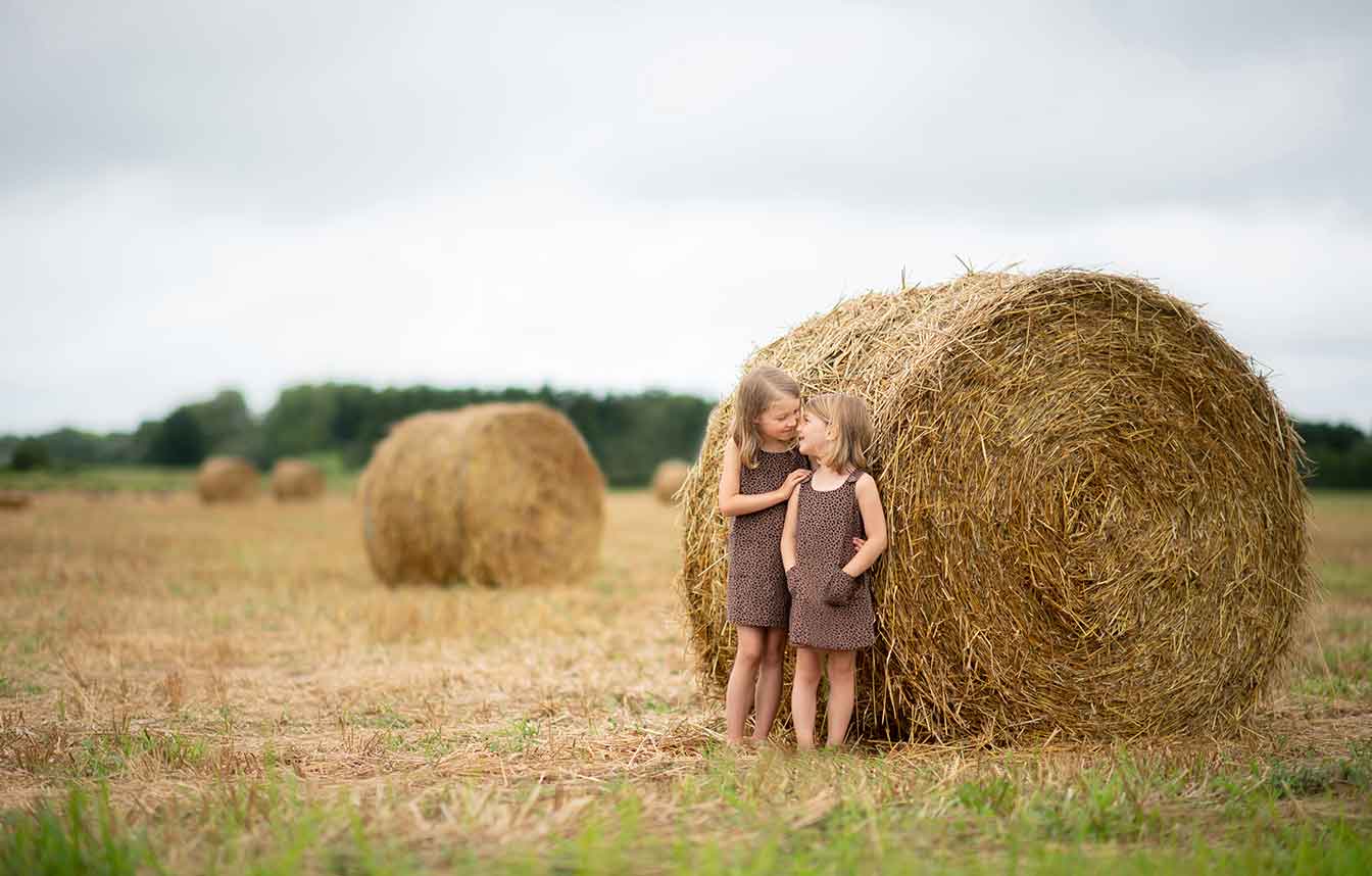 Two adorable girls in dresses standing near rolled hay in the Hamptons NY