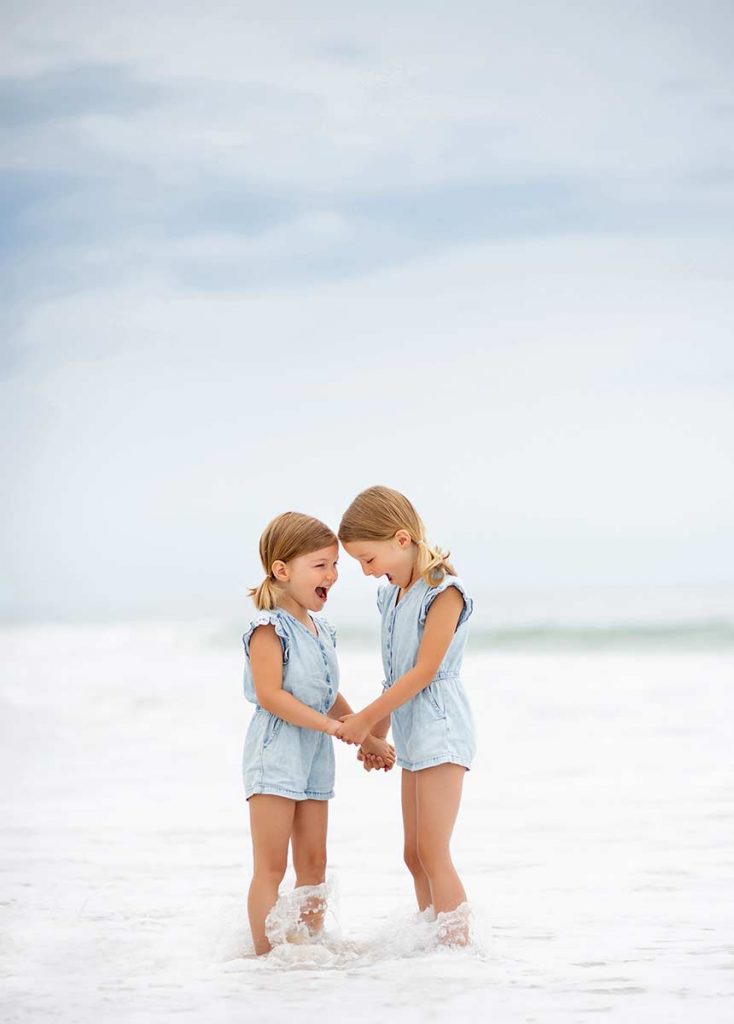 Sisters in denim dresses playing in the ocean in Hamptons NY