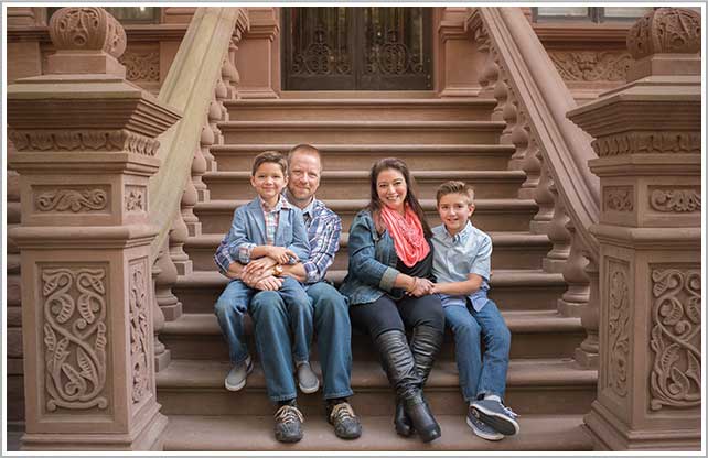 Parents, along with their two children, sit on a stoop of a brownstone in the Upper West Side neighborhood of NYC.