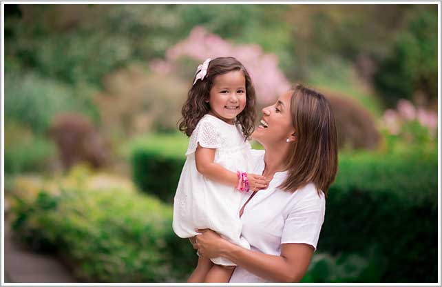 A happy mother holding her baby girl as they enjoy an afternoon at the Botanical Gardens in New York City.