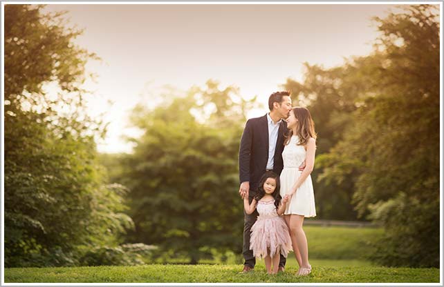 A married couple holding hands with their baby girl in a public park in New York City.