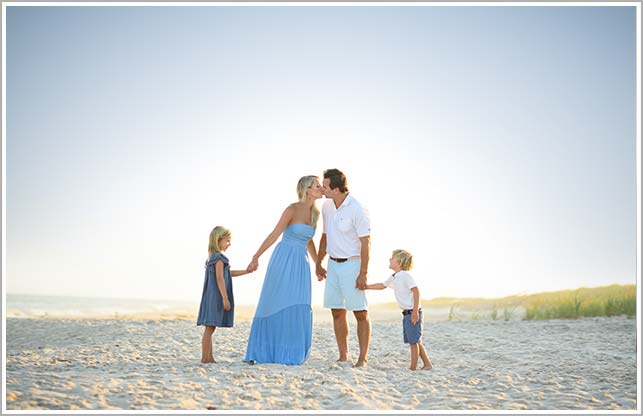 A mother and father kiss while they children smile in this family photo taken in the Hamptons, NY.
