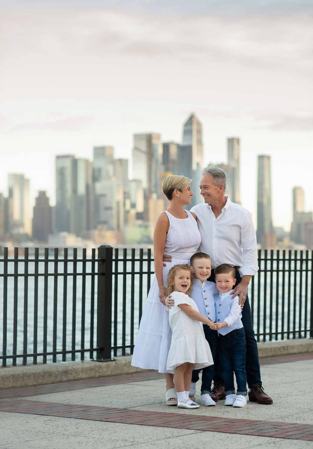 Parents cuddling children at the waterfront with NYC skyline views