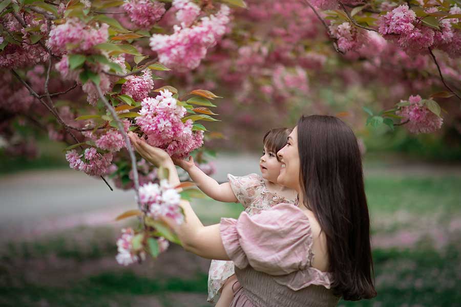 A mother holding her daughter while holding cherry blossoms in NYC's Central Park.