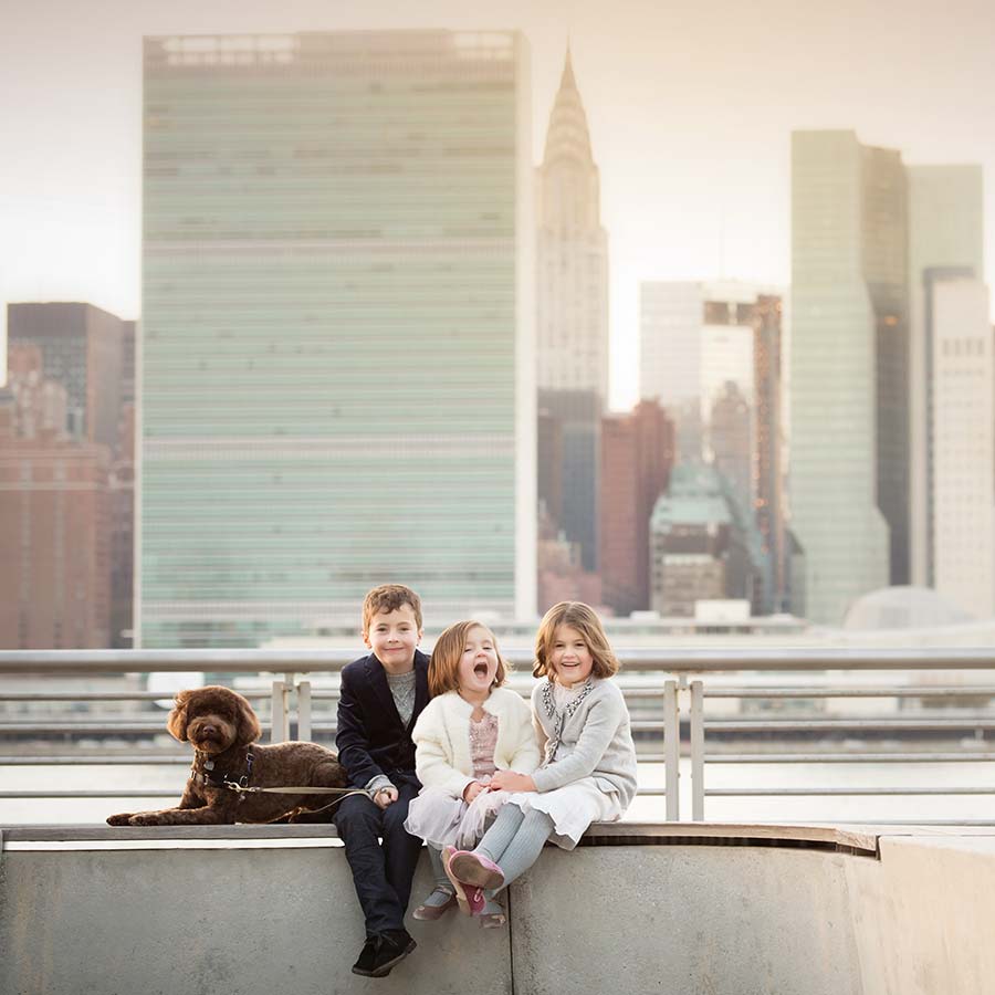 Three children and their pet dog posing for a photo on the NYC waterfront