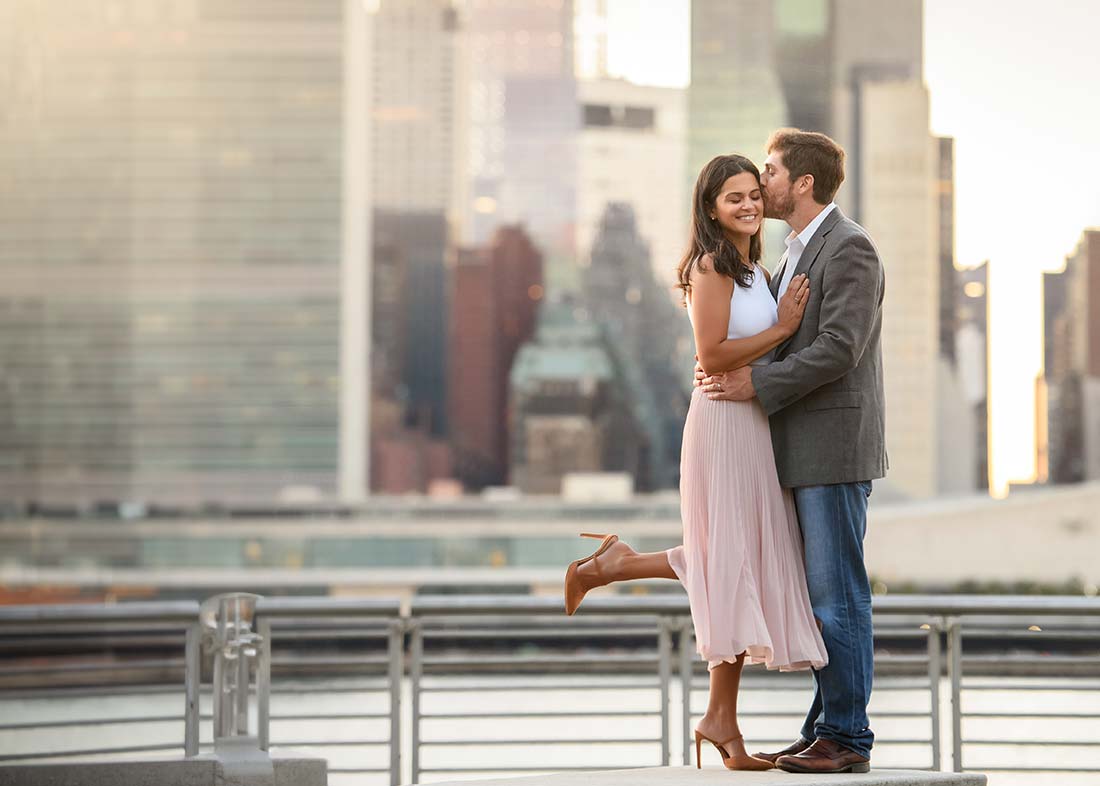 A husband and wife kiss on the NYC waterfront, with the iconic skyline as the backdrop