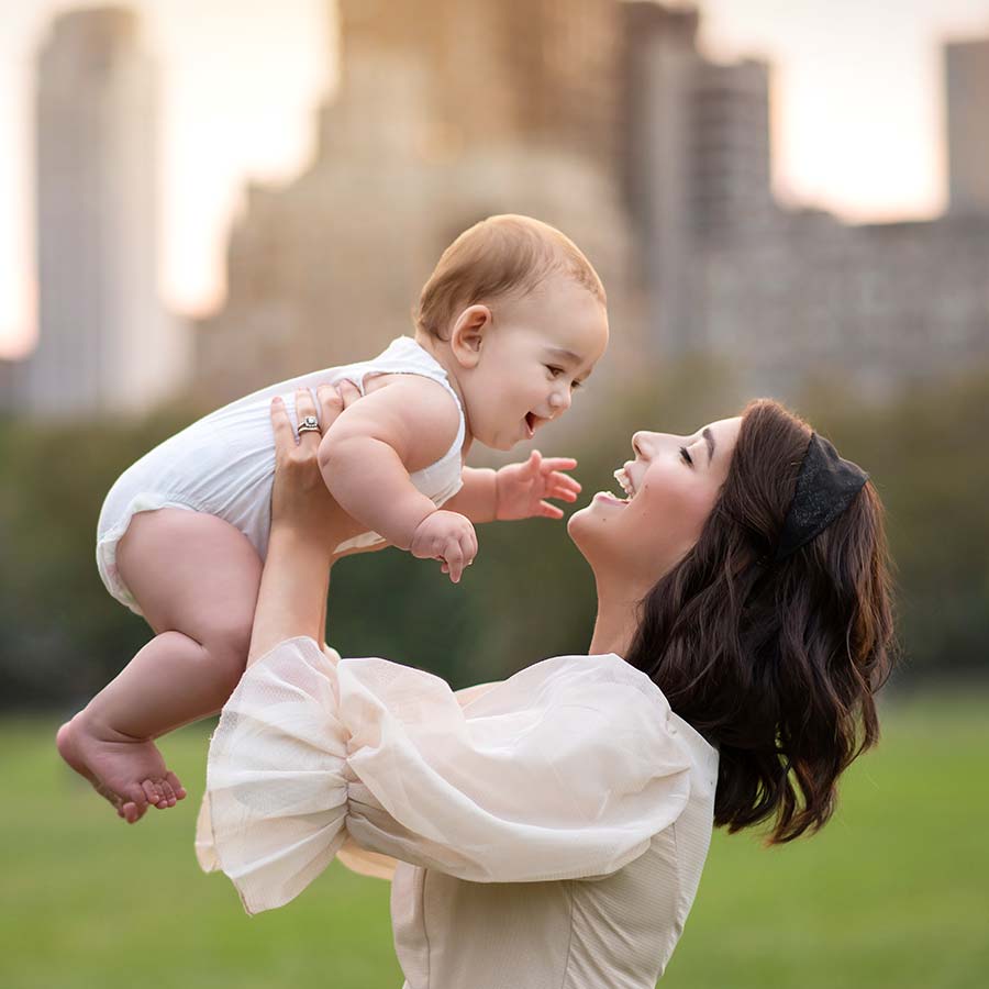 Mother holding up her baby in Central Park with NYC backdrop in the background